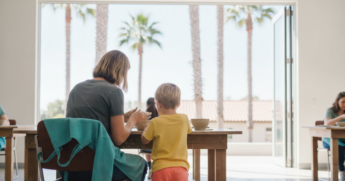 A parent and young child shape clay bowls at a wooden table in a sunlit studio
